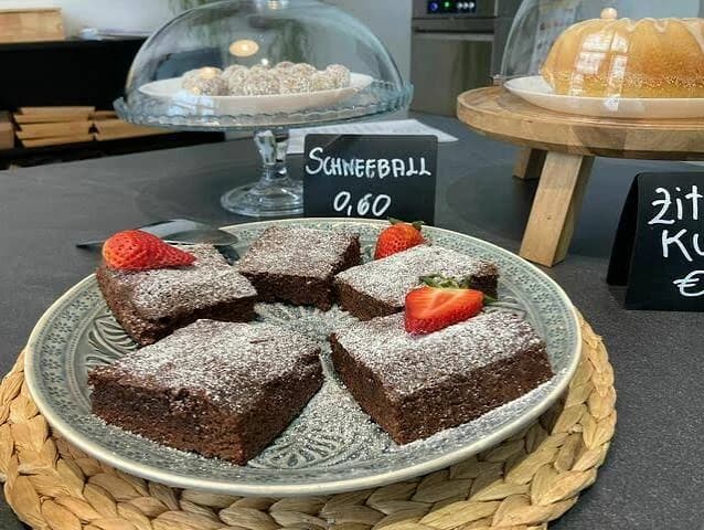 Brownies mit Staubzucker und Erdbeeren auf der Theke, dahinter Schneebälle und Kuchen unter Glashauben