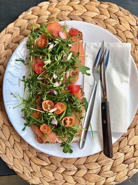Gegrilltes Sauerteigbrot mit Lachs, Rucola und Tomaten auf einem weißen Teller