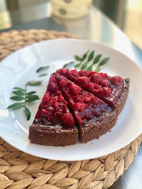 Ein Stück Kladdkaka mit frischen Himbeeren auf einem weißen Teller