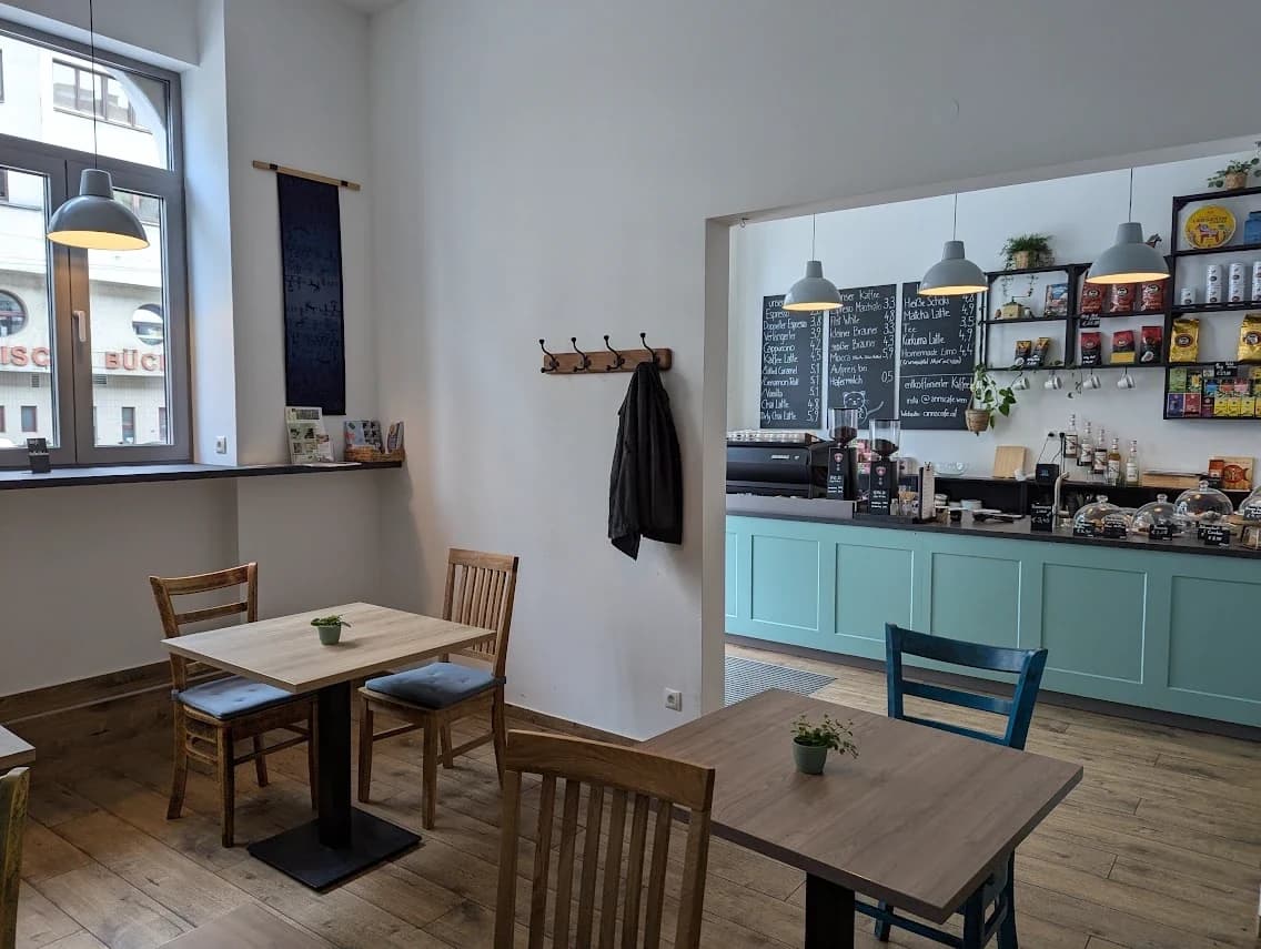 Innenraum von Anns Café: Holztische, Fenster zur Straße, mintgrüne Theke mit Gebäck und Kaffeemaschine