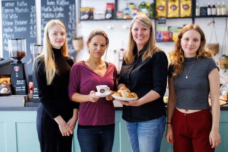 Vier Frauen hinter der Theke von Anns Café, mit Kaffee und Gebäck in der Hand
